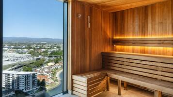 A sauna with wooden benches and a view of a cityscape through a large window.