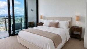 Quarto de hotel com uma cama grande, duas mesas de cabeceira, vista através de uma porta de vidro e uma varanda.