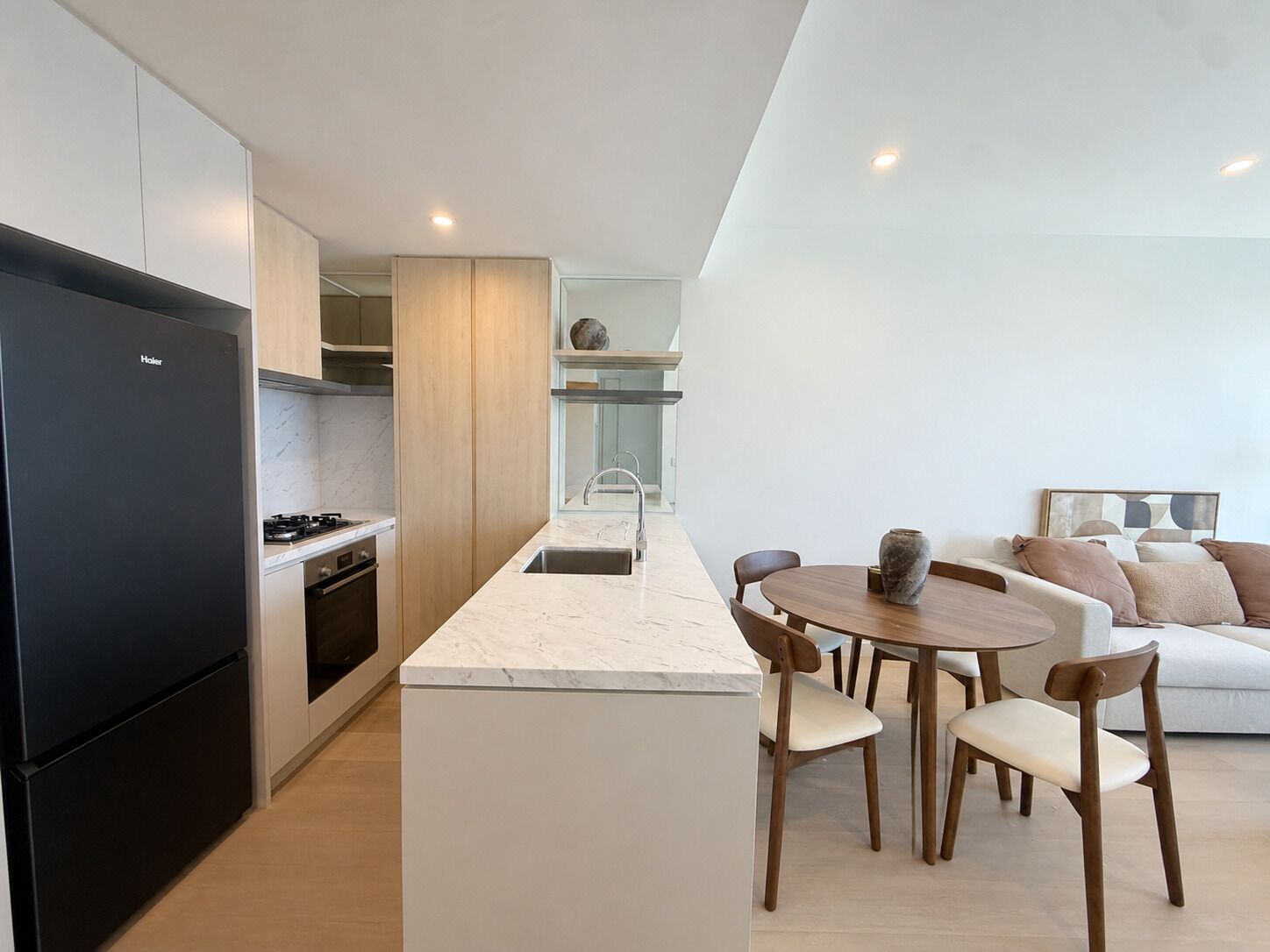 A modern kitchen with a black refrigerator, wooden cabinets, and a marble countertop.