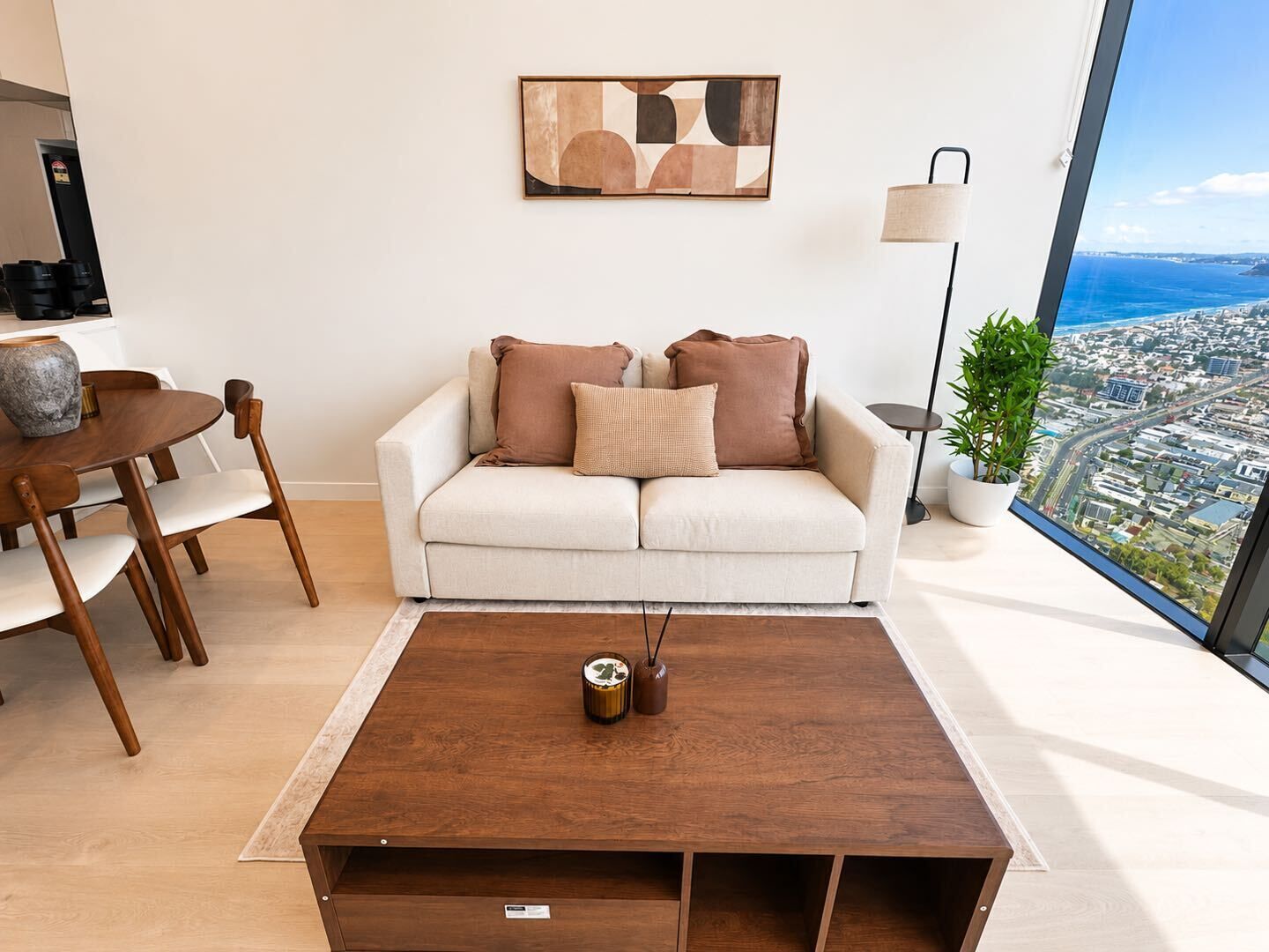 A modern living room with a sofa, coffee table, and a city view through a large window.