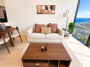 A modern living room with a sofa, coffee table, and a city view through a large window. - Vista in the Clouds - Coastal City Escape (Broadbeach)