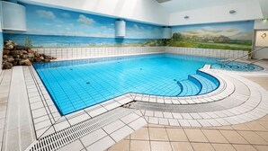 Una piscina amb un solàrium emblamat, un mural d'una escena de platja i un lucernari a sobre.