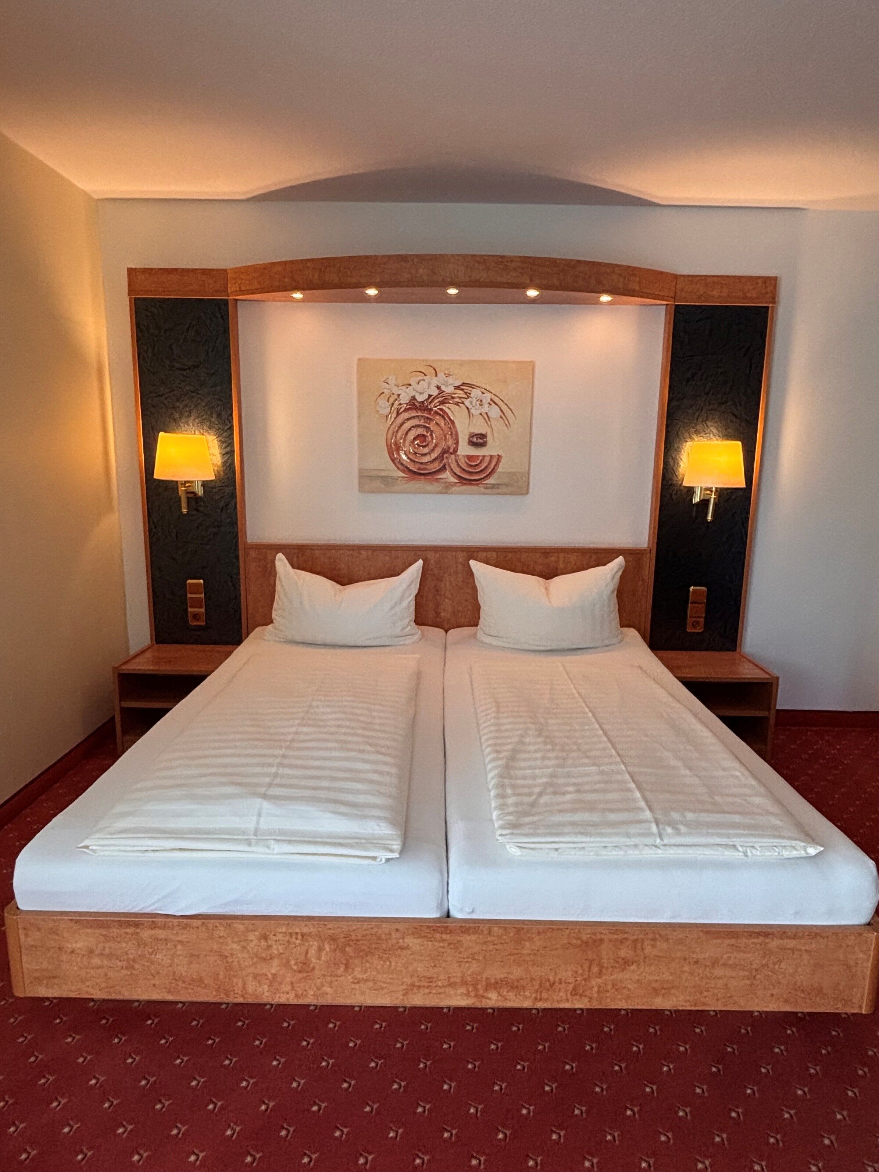 Una cama doble con cabecera de madera, dos mesitas de noche con lámparas y una obra de arte colgada en la pared.