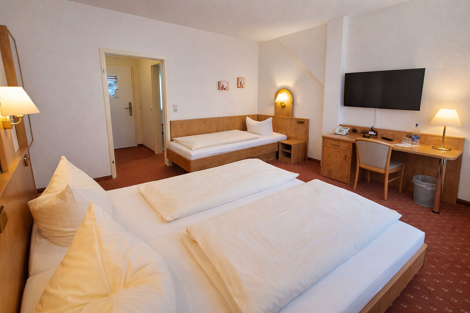 Een hotelkamer met twee bedden, een bureau, een stoel, een televisie en een prullenbak.