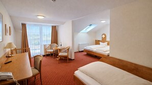 Habitació d'hotel amb un llit, una taula de nit amb un telèfon, una cadira, una taula i una finestra amb cortines.