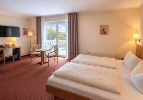 Ein Hotelzimmer mit einem Bett, einem Schreibtisch, einem Stuhl, einem Fernseher und einem Fenster mit Vorhängen.