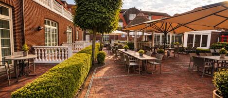 An outdoor patio area with brick flooring, tables, chairs, and umbrellas.
