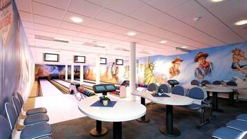 A bowling alley with multiple lanes, seating areas, and a mural of a cowboy on the wall.