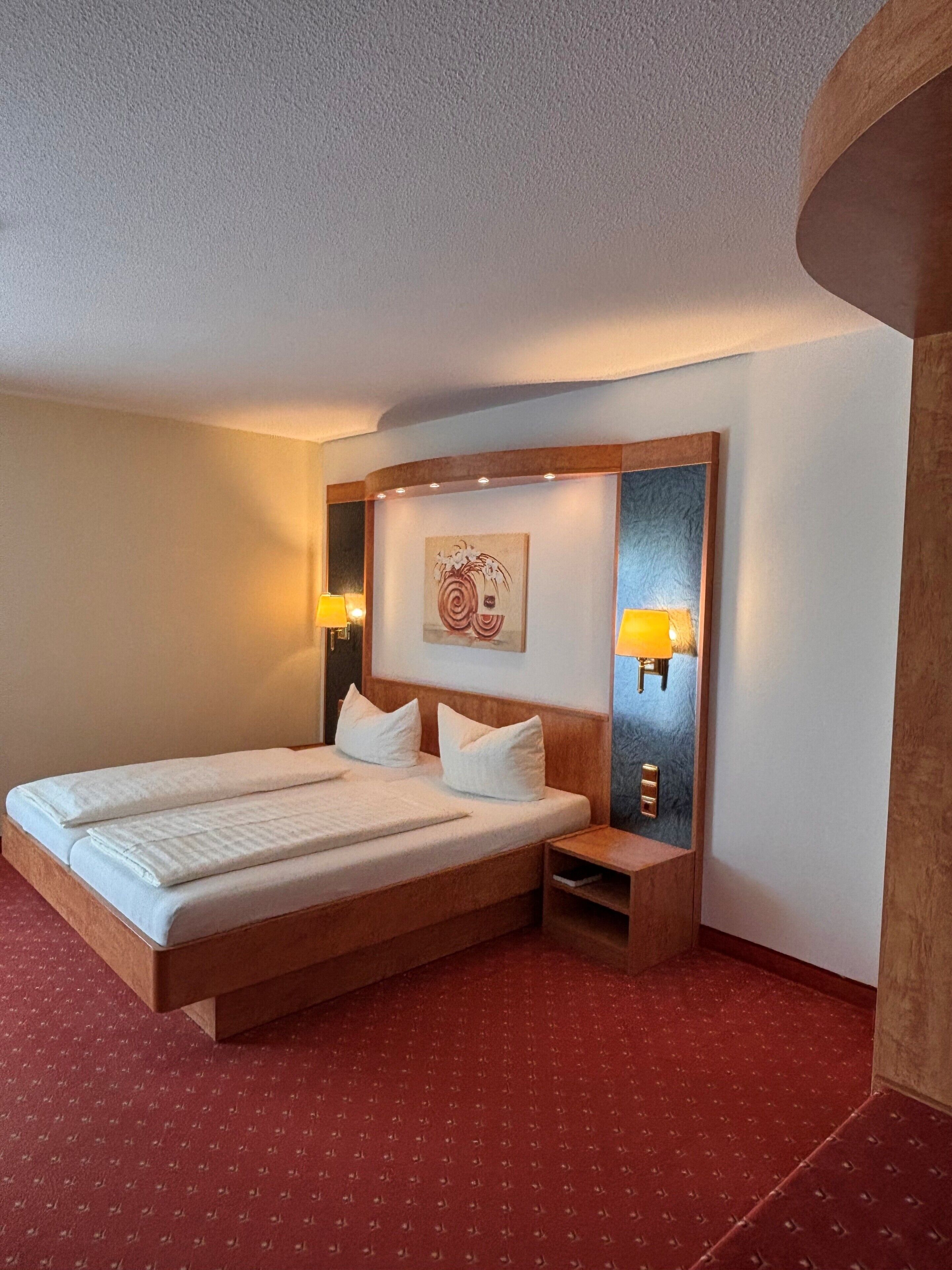 A hotel room with a double bed, two bedside tables, a headboard, and a wall-mounted artwork.