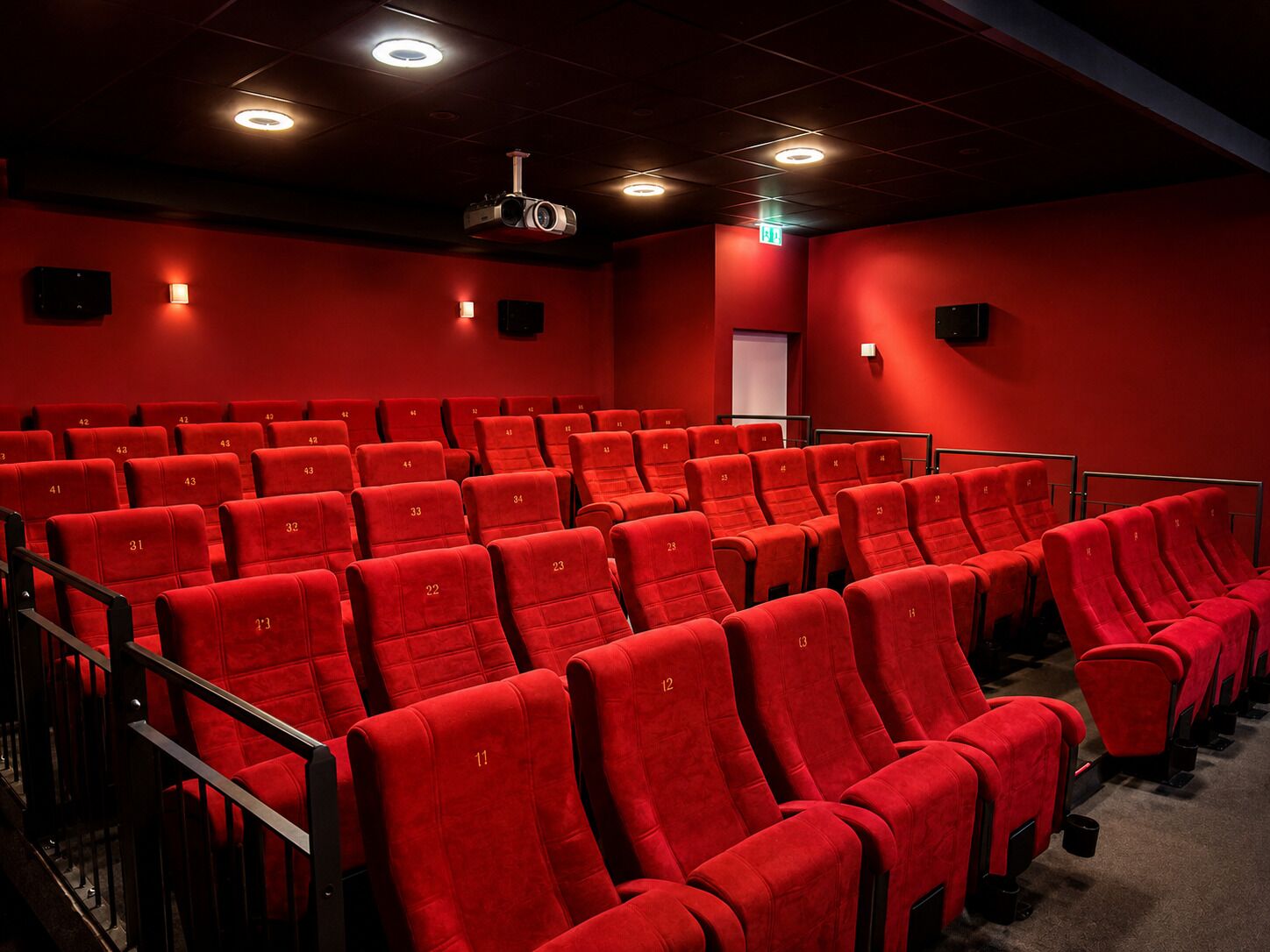 A theater with rows of red seats, a projector, and a red wall.