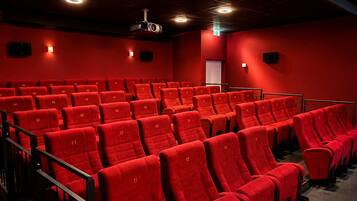 A theater with rows of red seats, a projector, and a red wall.