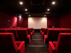 A theater with rows of red seats, a large screen, and a stage with curtains.