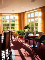 Ein Zimmer mit rotem Teppich, verschiedenen Sitzmöglichkeiten und großen Fenstern mit Vorhängen.