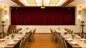 Ett konferensrum med en scen, flera bord uppställda för servering och ett parkettgolv i fiskbensmönster.