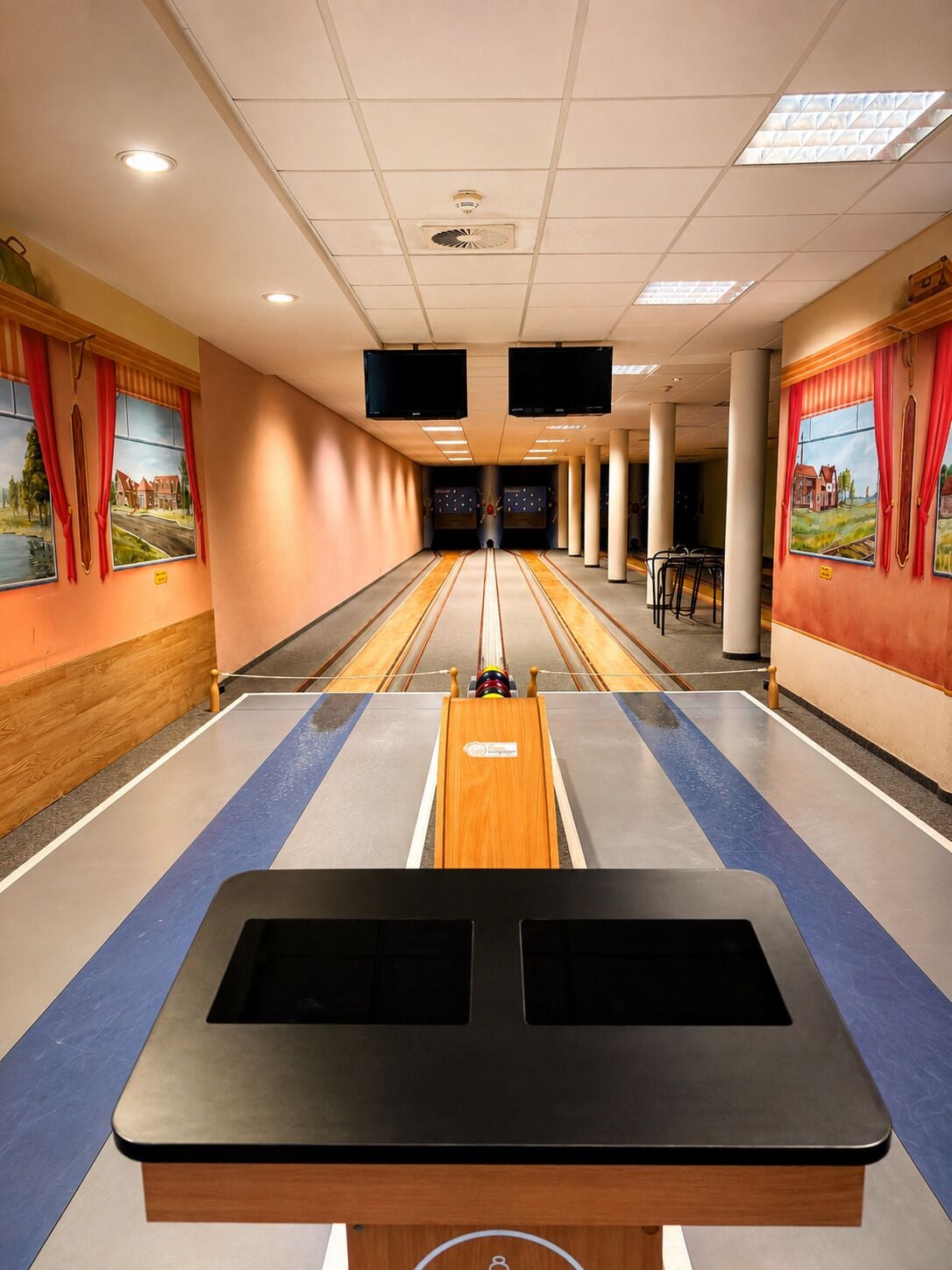 A bowling alley with a wooden bowling lane, two black bowling balls, and a pinsetter.