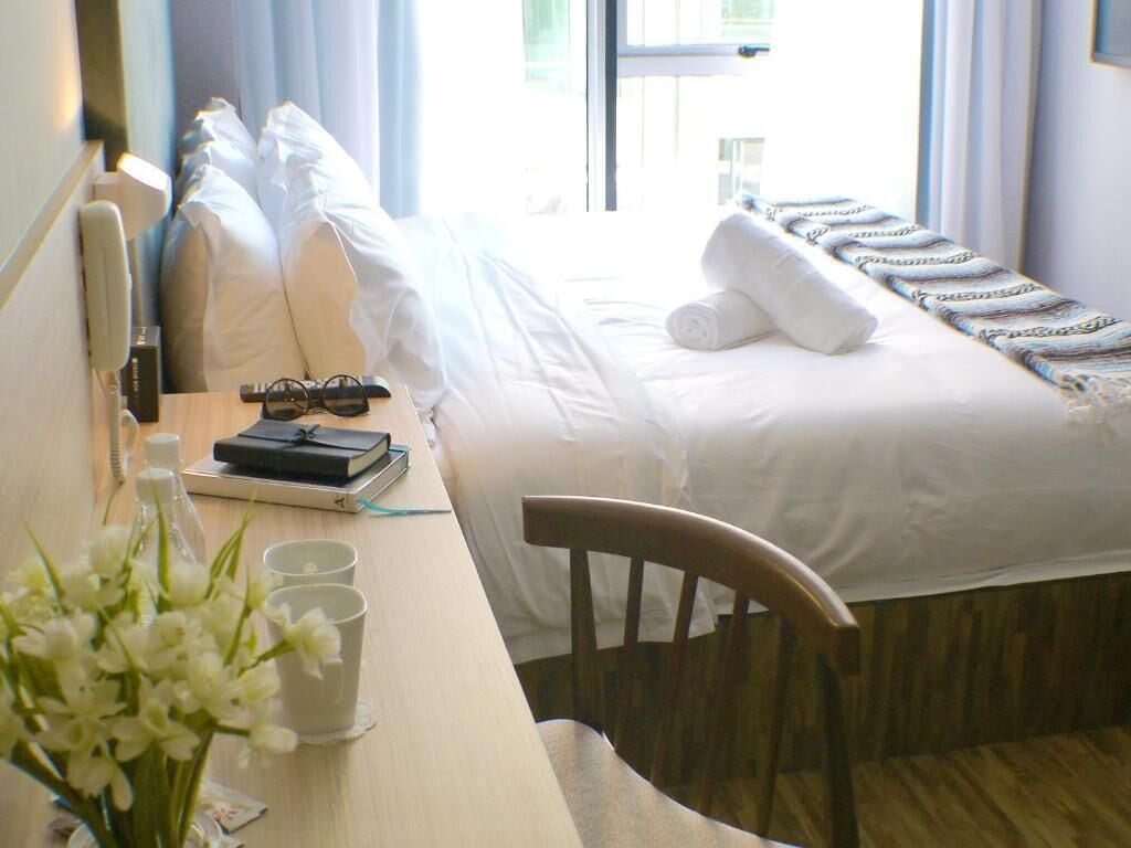 Habitación de hotel con cama, escritorio, silla, florero y ventana con cortinas.