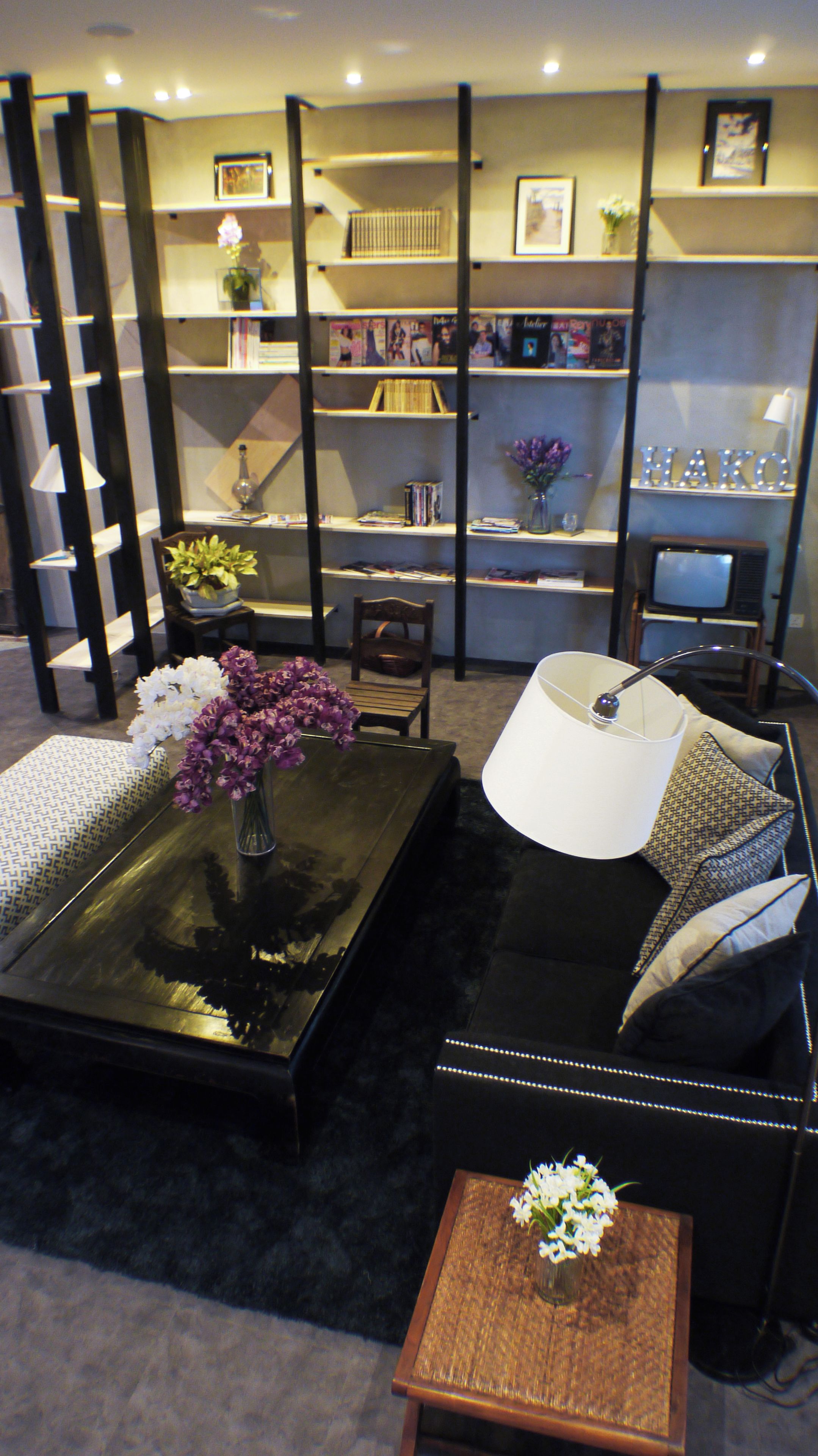 A modern living room with a black sofa, a coffee table with a vase of flowers, a bookshelf, and a television.