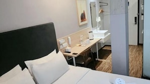 Una habitación de hotel con una cama, un escritorio, una silla, un espejo y una puerta.