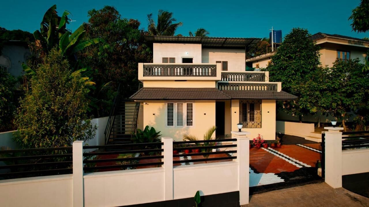 Une maison moderne à deux étages, dotée d’un balcon et entourée d’une végétation luxuriante.