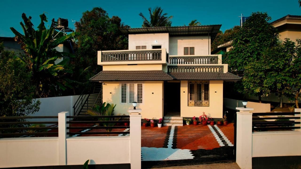 Una casa de dos pisos con balcón, escalera y jardín con plantas en macetas.