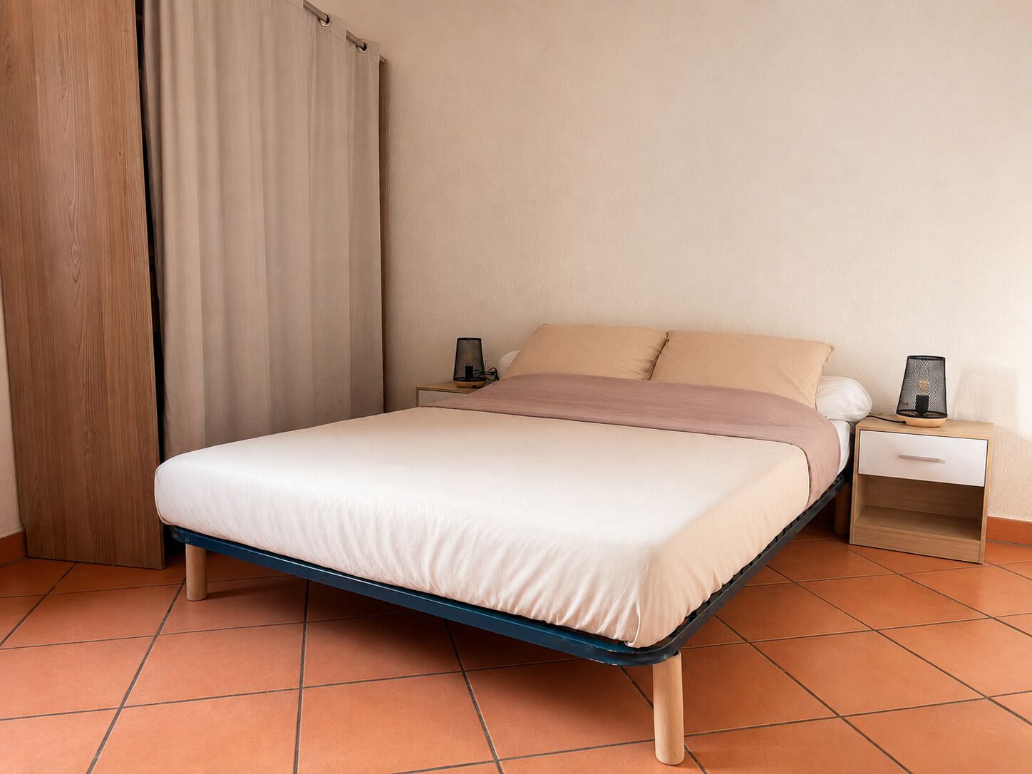 Un letto singolo con struttura in legno, un comodino con una lampada e una tenda.