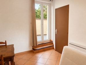 Una habitació amb una taula de fusta, un sofà blanc, una porta i una finestra amb cortines.