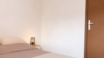 Een slaapkamer met een bed, nachtkastje, lamp en een deur.