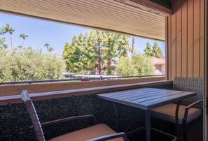 Uma varanda com mesa e cadeiras, com vista para uma rua arborizada.