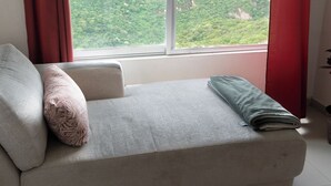 A room with a sofa, a window with red curtains, and a view of a green landscape.