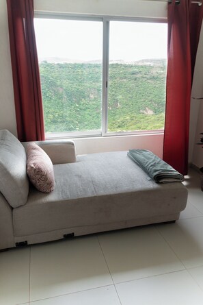 A room with a sofa, a window with red curtains, and a view of a green landscape.
