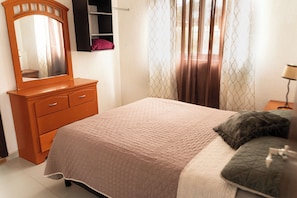 A bedroom with a bed, a dresser, a mirror, and a window with curtains. - Vrbo Property (Tonalá)