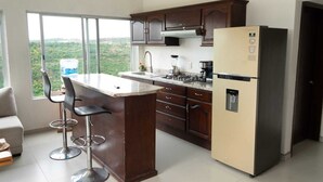 A kitchen with a bar area, a refrigerator, and a window with a view of greenery.