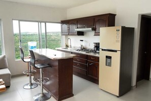 A kitchen with a bar area, a refrigerator, and a window with a view of greenery.