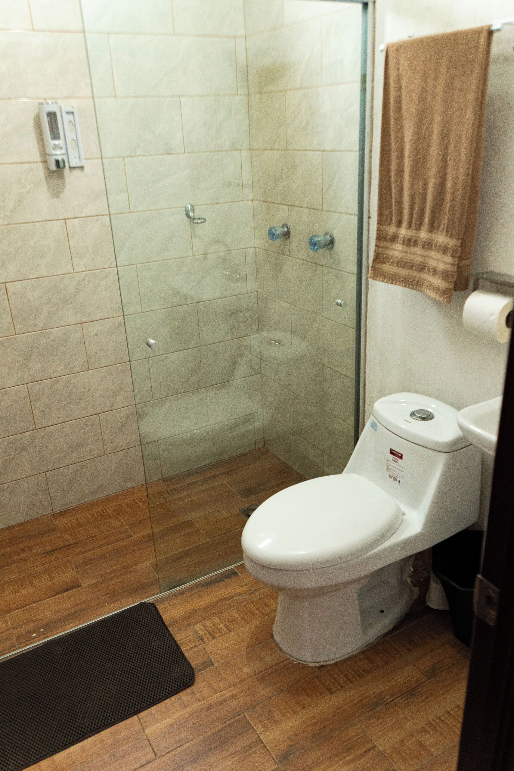 Un baño con cabina de ducha de vidrio, un inodoro y una toalla colgada en la pared.