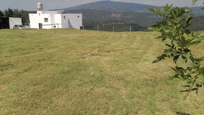A grassy field with a white building, a car, and a mountain in the background.