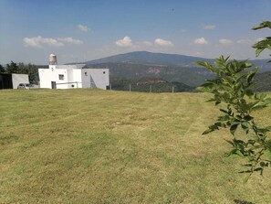 A grassy field with a white building, a car, and a mountain in the background.
