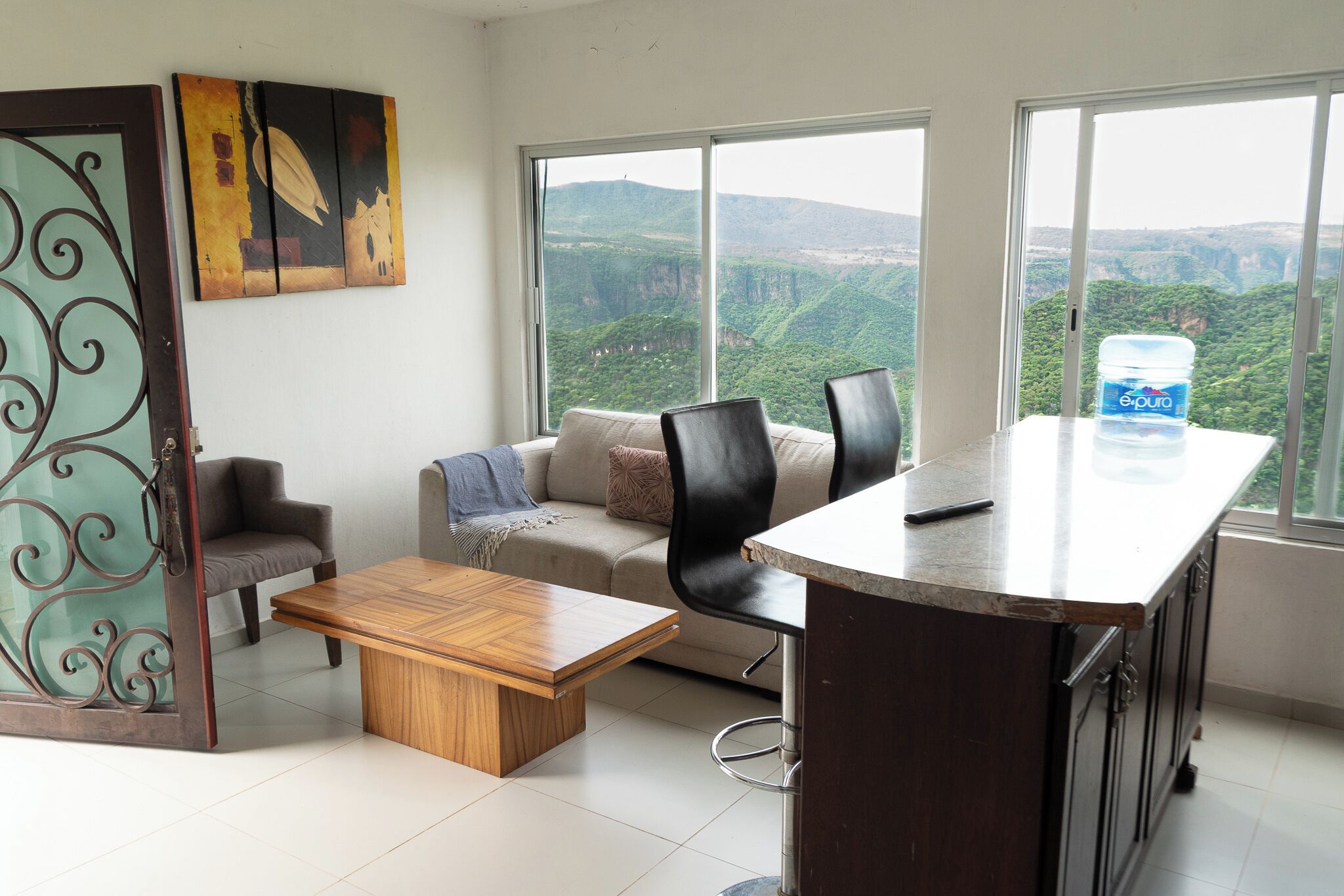 Un salon moderne avec un canapé, une table basse et un coin repas doté d’un bar. De grandes fenêtres offrent une vue sur un paysage montagneux.