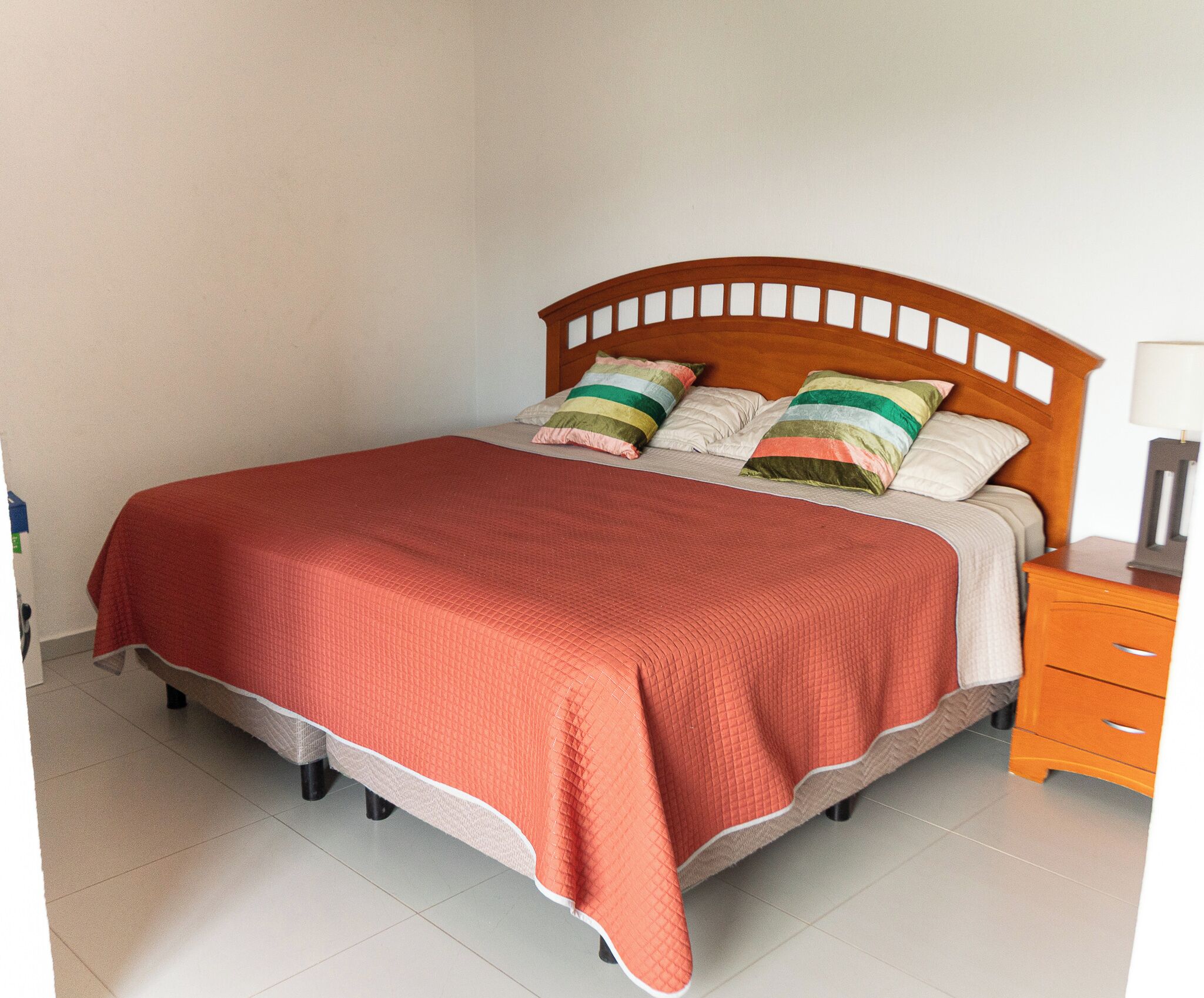 A bed with a wooden headboard, a red blanket, and two pillows with striped patterns.