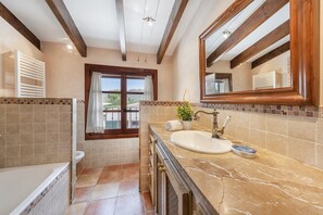 A bathroom with a marble sink, a window with curtains, and a view of greenery outside. - Grand Majorcan Retreat With Pool (Pollença)