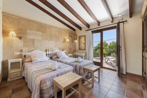 A bedroom with two beds, a small table, and a balcony with a view. - Grand Majorcan Retreat With Pool (Pollença)