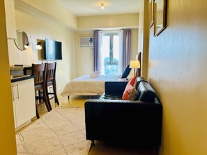 A compact hotel room with a kitchenette, a bed with a view, a sofa, and a TV. - Studio Suite Condo at the Avida Towers Abreeza in vibrant Davao City (Davao City)