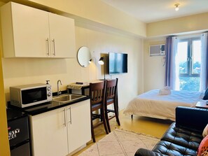Habitación de hotel compacta con kitchenette, una cama, televisor y vista al exterior.
