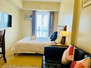A hotel room with a bed, a desk, a chair, a TV, and a window with curtains.