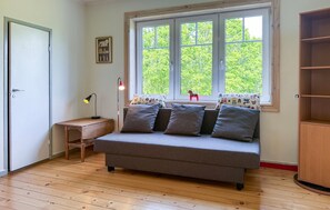 A room with a grey sofa, a wooden desk, a lamp, and a window with a view of trees. - Awesome home in Lammhult with WiFi (Lammhult)
