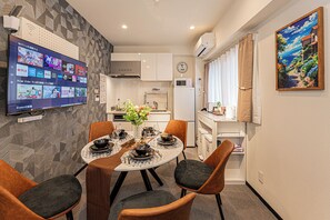 A modern dining area with a round table set for four, a kitchen in the background, and a wall-mounted TV displaying streaming services. - Kiyoka Ryokan Shinkoiwa No.2 (Katsushika-ku)