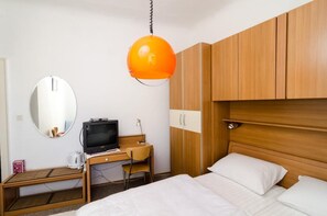 Ein Hotelzimmer mit einem Bett, einem Schreibtisch mit Fernseher, einem Sessel, einem Kleiderschrank und einer Pendelleuchte.