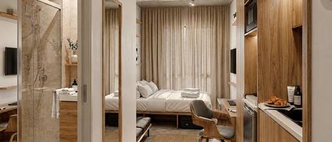 A compact hotel room with a bed, desk, chair, and a shower area.