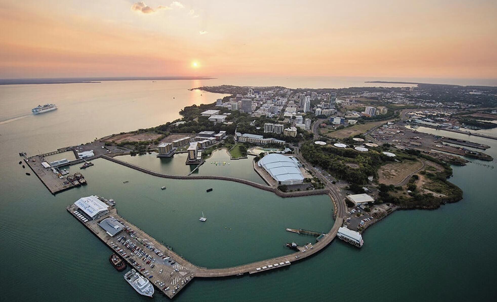Vista aérea de una ciudad costera con un puerto deportivo, un estadio grande y una zona urbana densa.