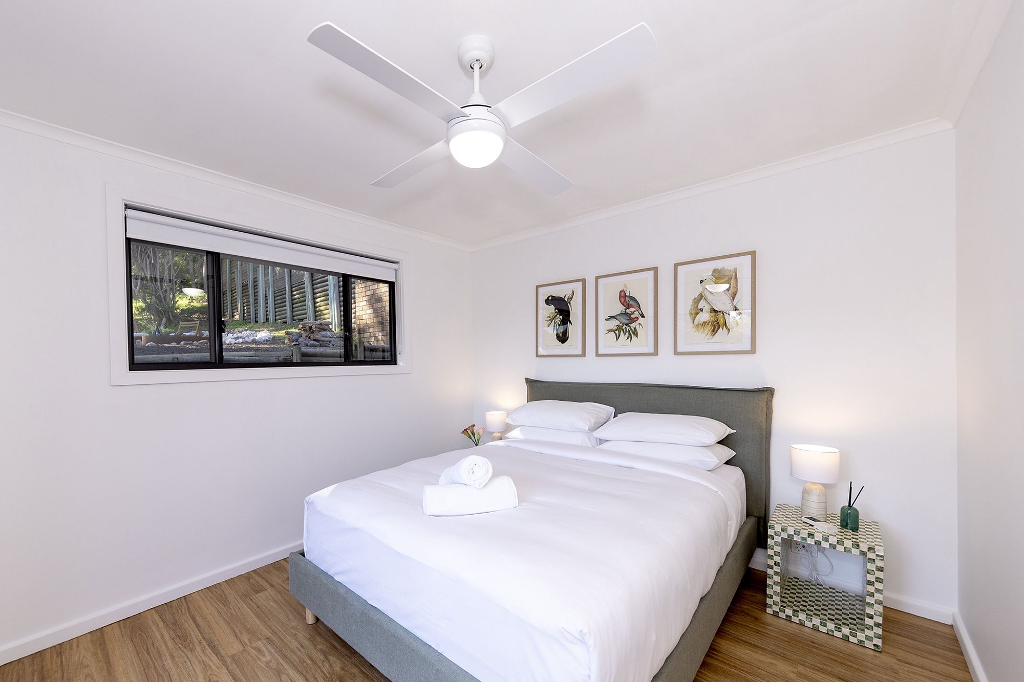 A neatly made bed with white linens, a ceiling fan, and framed wall art.