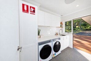 A modern laundry room with white cabinets, a sink, and two front-loading washing machines.